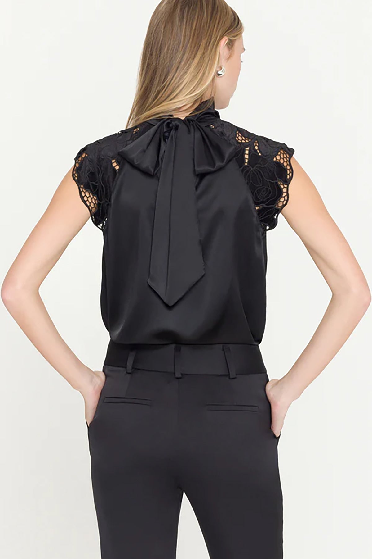 Black sleeveless top with lace details and a bow tie, worn by a person on a white background