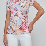 Woman wearing a colorful patterned top with white pants on a plain background
