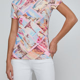 Woman wearing a colorful patterned top with white pants on a plain background
