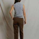 Person wearing a sleeveless gray top and brown pants against a plain background