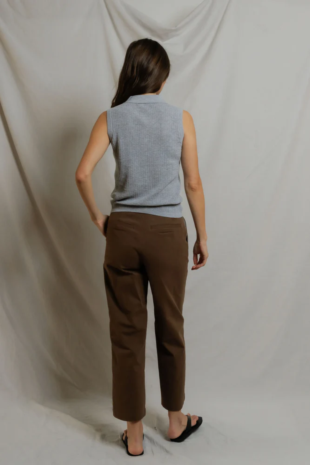 Person wearing a sleeveless gray top and brown pants against a plain background