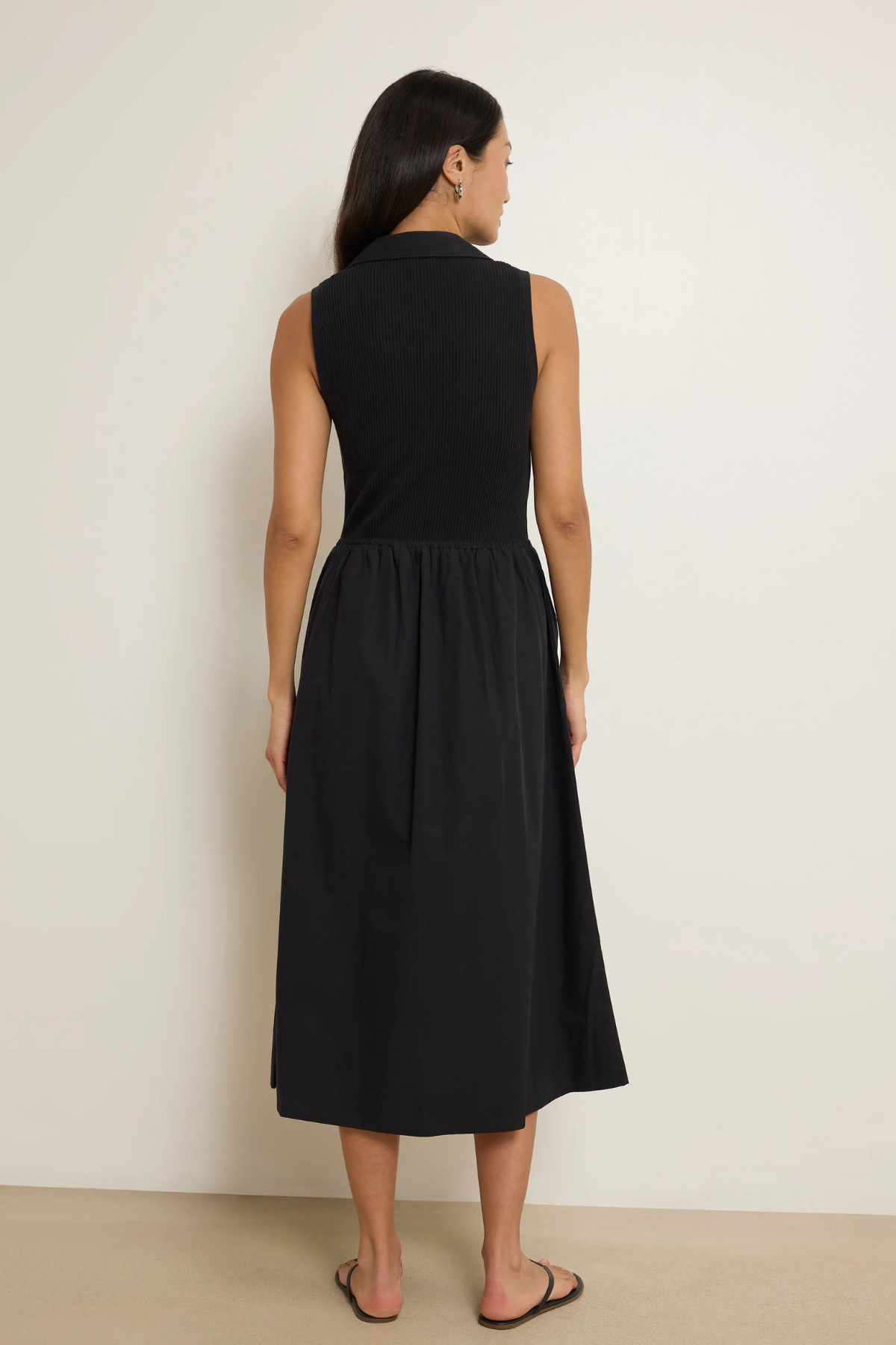 Woman wearing a black sleeveless dress against a plain background