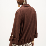 A model shown from the back wearing a textured brown crinkled jacket with rolled cuffs and a zebra-print skirt, against a plain white background.