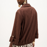 A model shown from the back wearing a textured brown crinkled jacket with rolled cuffs and a zebra-print skirt, against a plain white background.