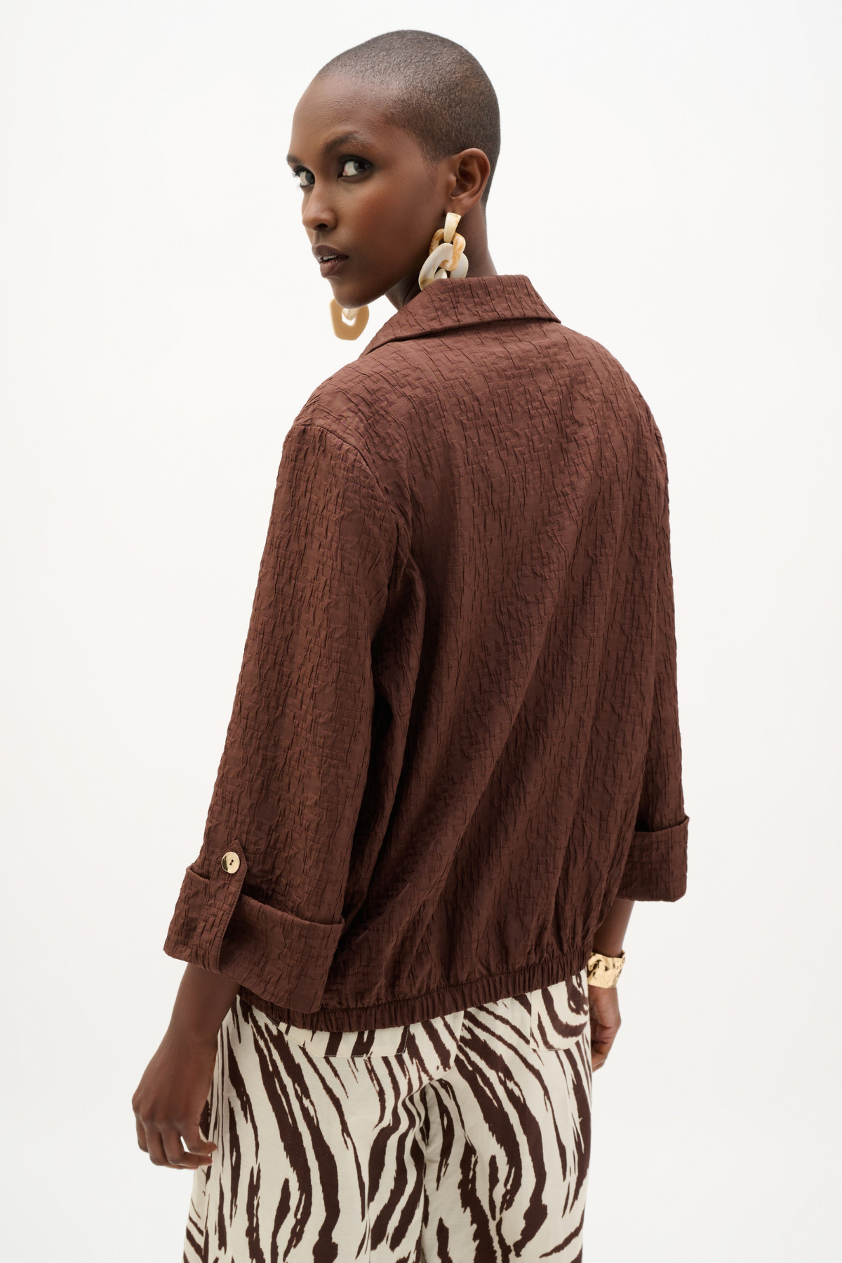 A model shown from the back wearing a textured brown crinkled jacket with rolled cuffs and a zebra-print skirt, against a plain white background.