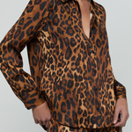 A model wearing a matching leopard-print long-sleeve button-up shirt and trousers set, shown from the neck down against a light gray studio background.