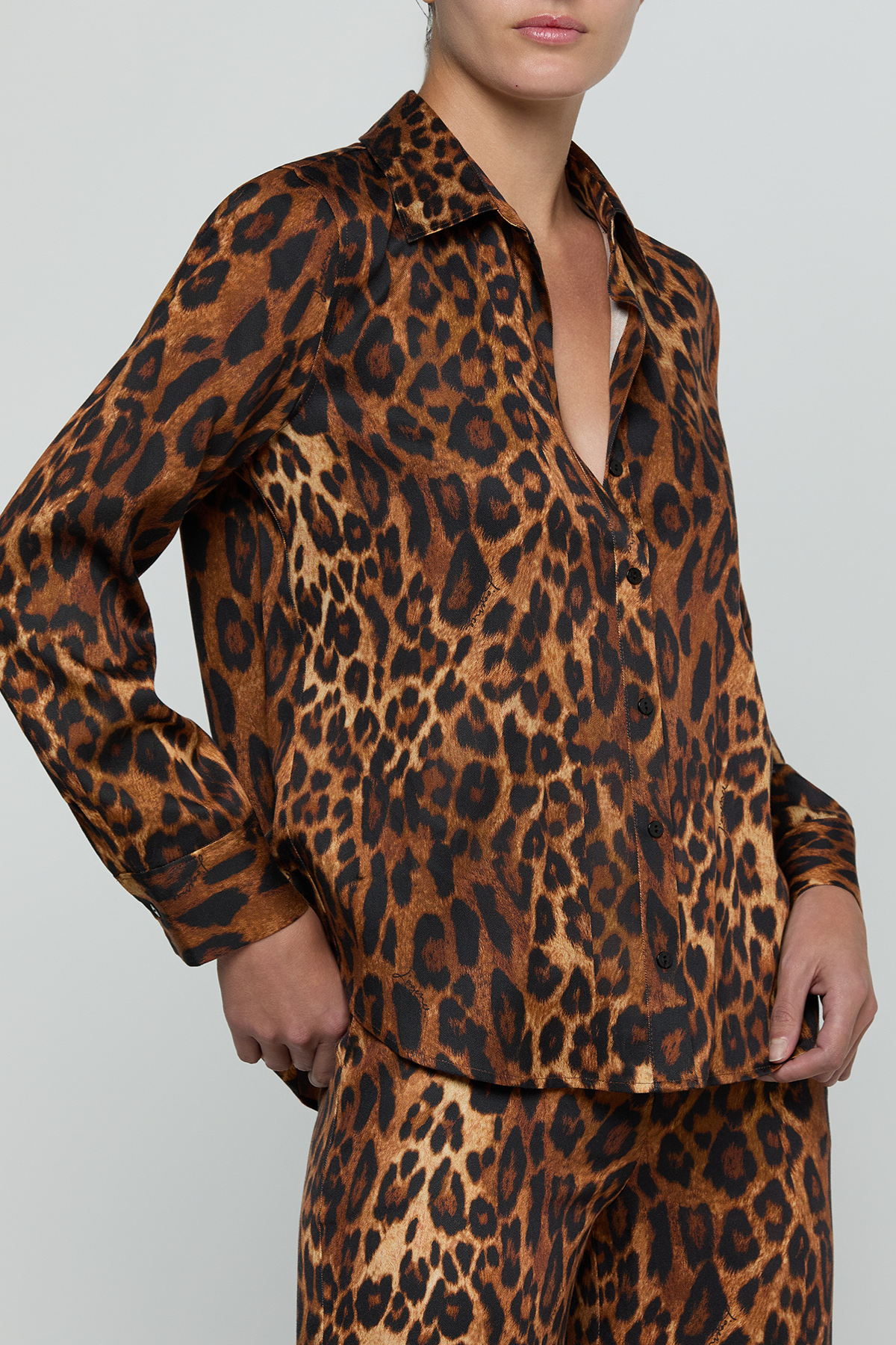 A model wearing a matching leopard-print long-sleeve button-up shirt and trousers set, shown from the neck down against a light gray studio background.