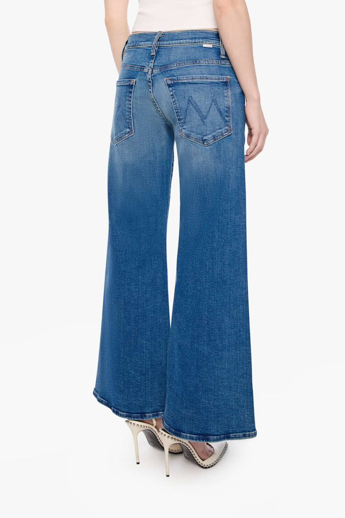 A model shown from the back wearing blue wide-leg flare jeans with a faded wash and silver high-heeled studded heels, against a plain white background.