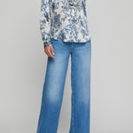 Person wearing a floral blouse and blue jeans on a gray background