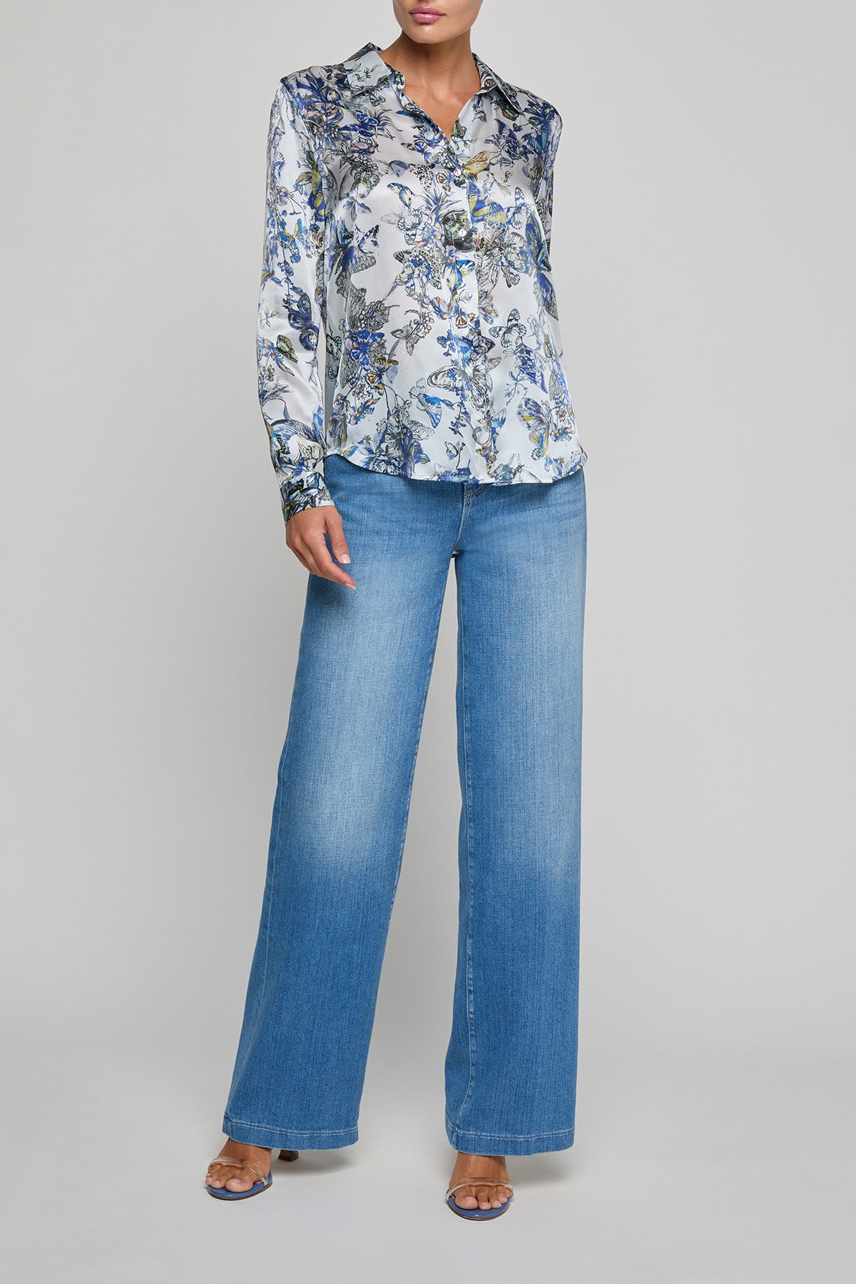 Person wearing a floral blouse and blue jeans on a gray background