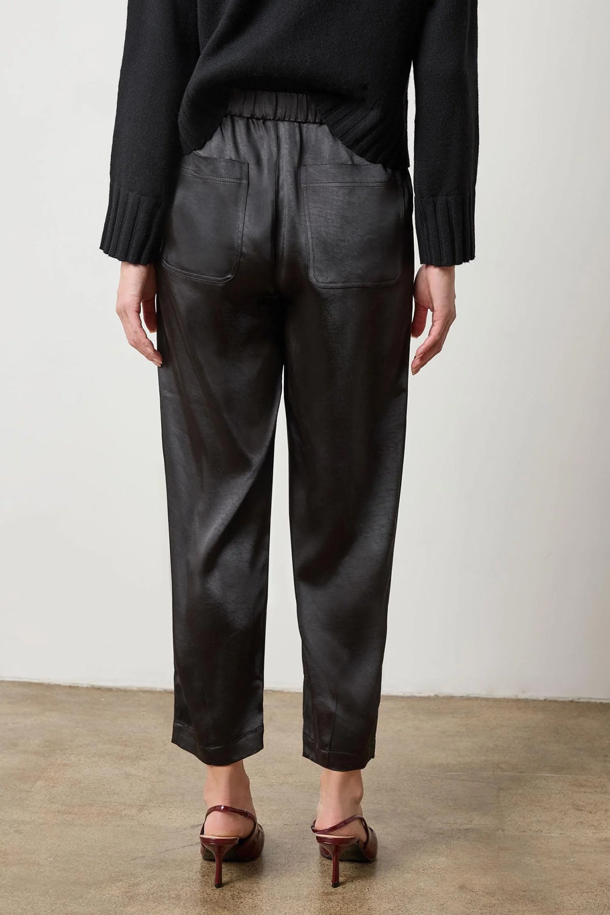 Black satin straight-leg pant with fly-front closure, styled with heels
