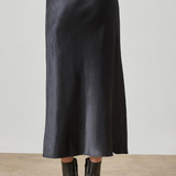 A black satin midi skirt worn by a model, shown from the back against a neutral studio background with a concrete floor.