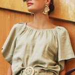 Woman wearing a green outfit with sunglasses and earrings against a textured wall.