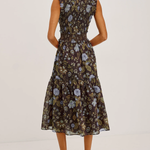 A woman modeling a sleeveless midi dress with a ruffled neckline and a tiered skirt, shown from the back. The dress features a dark brown base with a blue and beige floral pattern.