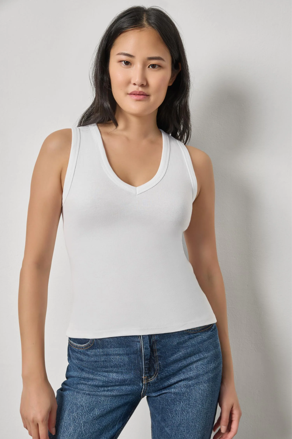 Model wearing a white sleeveless V-neck knit tank with blue denim.