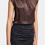 A woman wearing a sleeveless high-neck top in dark brown satin with sheer lace shoulder panels, paired with a dark ruched skirt, against a light gray studio background.