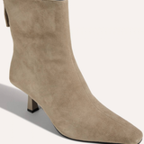 A taupe suede ankle boot with a pointed toe and a low block heel, shown from a three-quarters angle on a light beige background.
