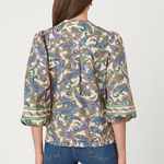 Woman wearing a patterned blouse and jeans on a plain background