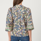 Woman wearing a patterned blouse and jeans on a plain background