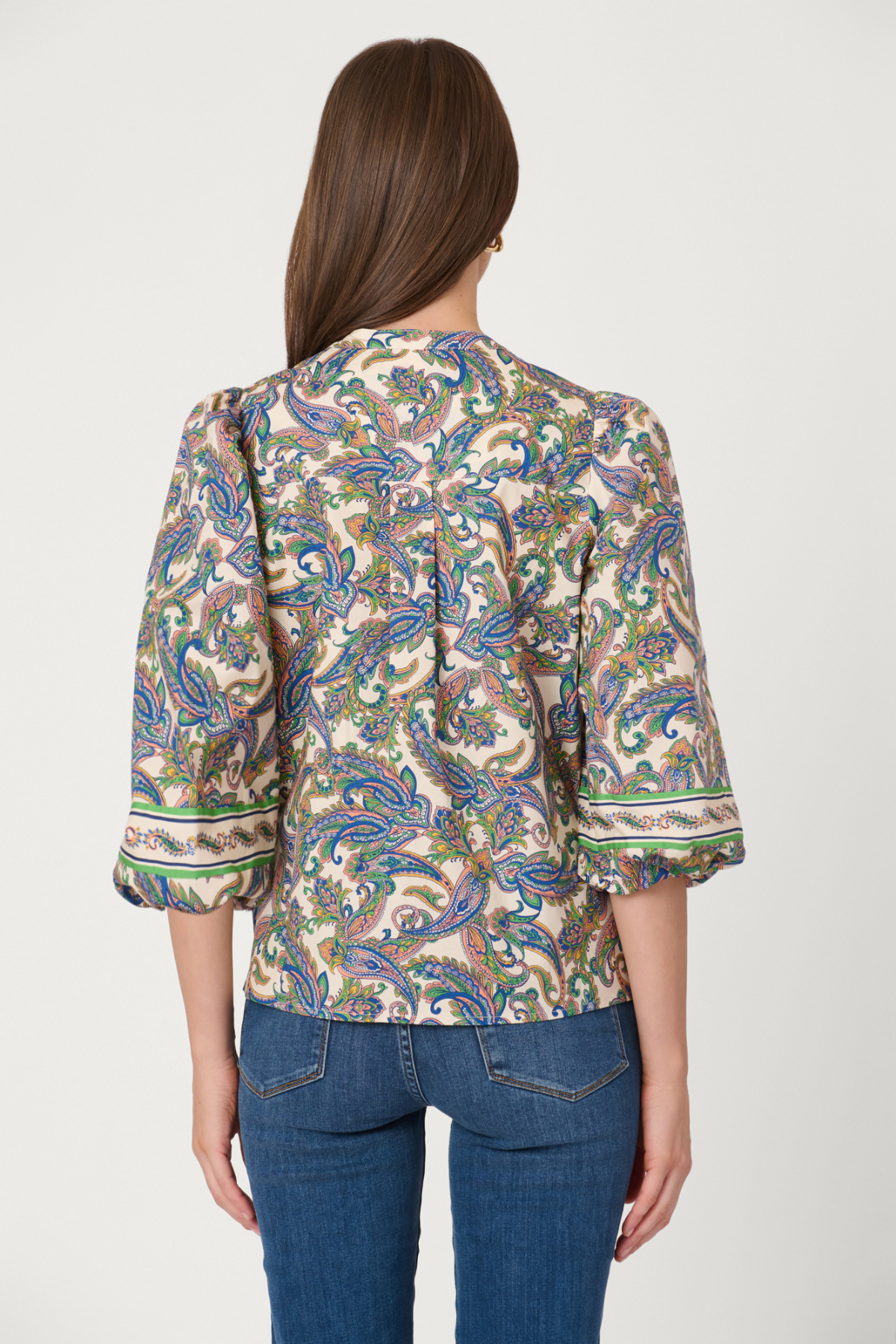 Woman wearing a patterned blouse and jeans on a plain background