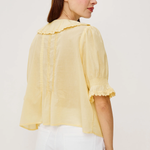 Woman wearing a light yellow blouse with ruffled details on a white background