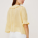 Woman wearing a light yellow blouse with ruffled details on a white background