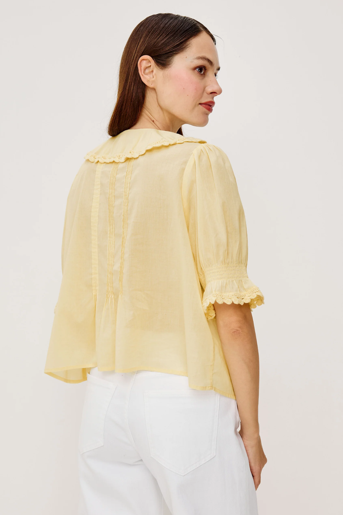 Woman wearing a light yellow blouse with ruffled details on a white background