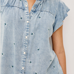 Light blue denim shirt with decorative embellishments on a plain background