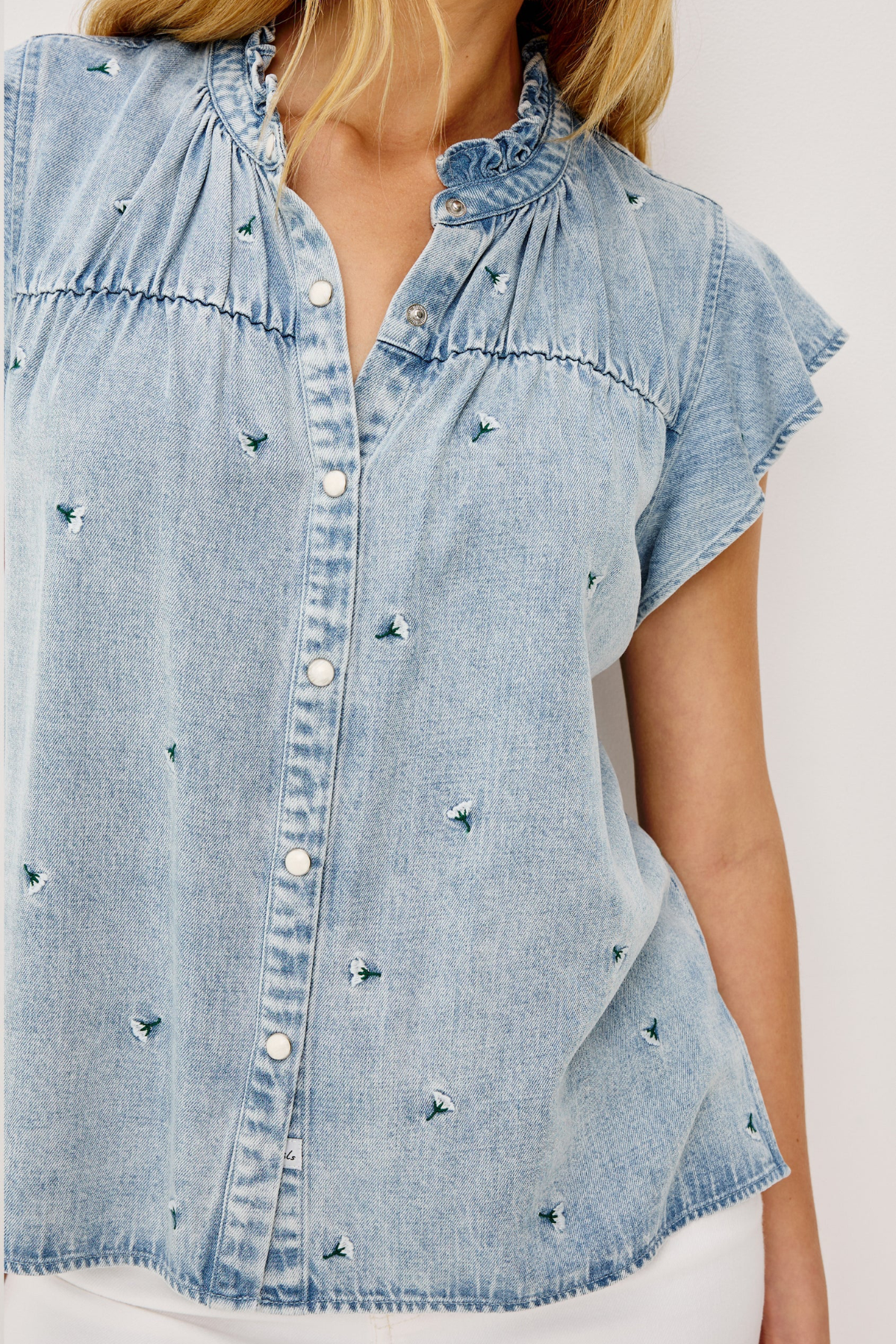 Light blue denim shirt with decorative embellishments on a plain background