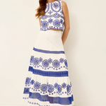 Woman wearing a white dress with blue floral patterns on a plain background