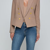 Person wearing a beige blazer with gold buttons and blue jeans on a light gray background