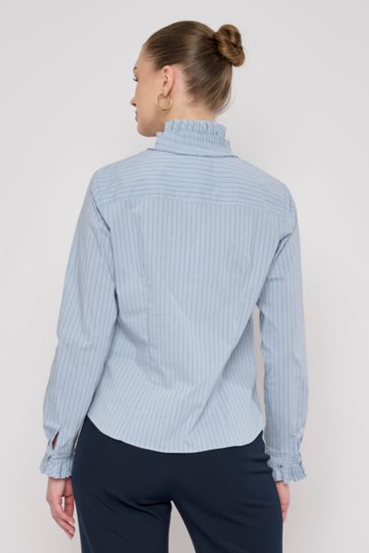 Model wearing a striped long-sleeve blouse with ruffle detailing and a relaxed, polished silhouette.