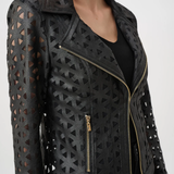 A close-up of a model wearing a black leather motorcycle jacket with geometric laser-cutout patterns and gold-tone zippers.