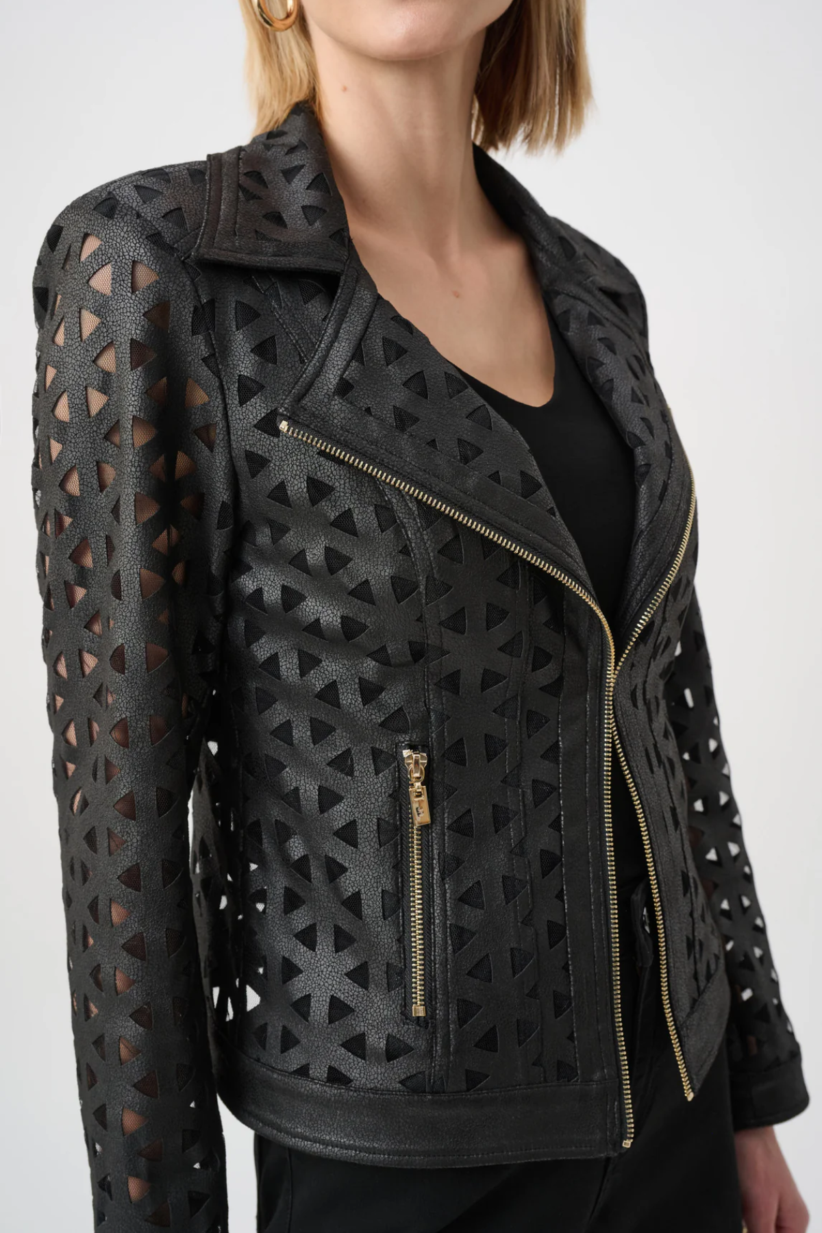 A close-up of a model wearing a black leather motorcycle jacket with geometric laser-cutout patterns and gold-tone zippers.