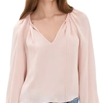 A woman wearing a light pink long-sleeve blouse with a gathered V-neckline and drawstring details, paired with blue jeans, against a plain white background.