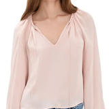 A woman wearing a light pink long-sleeve blouse with a gathered V-neckline and drawstring details, paired with blue jeans, against a plain white background.