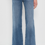 A person wearing medium-wash blue wide-leg flare jeans with a faded wash, paired with beige woven flat shoes, shown from the waist down against a plain white studio background.