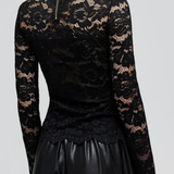 A woman shown from the back wearing a black long-sleeve lace top with a high mock neck and a small gold zipper at the collar, paired with black pants, against a light gray studio background.