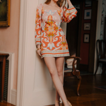 Woman in a colorful dress standing in a room with a fireplace and artwork.