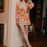 Woman in a colorful dress standing in a room with a fireplace and artwork.