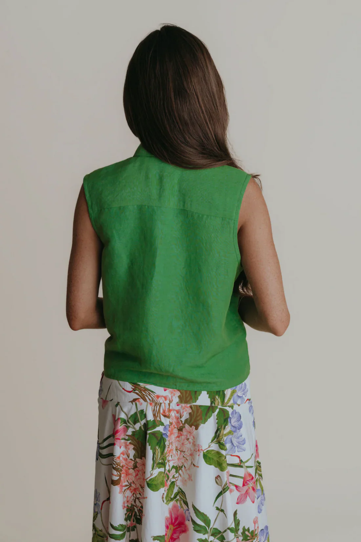 Person wearing a green sleeveless top with floral pants on a plain background