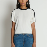 Woman wearing a white t-shirt with black accents and blue jeans on a plain background