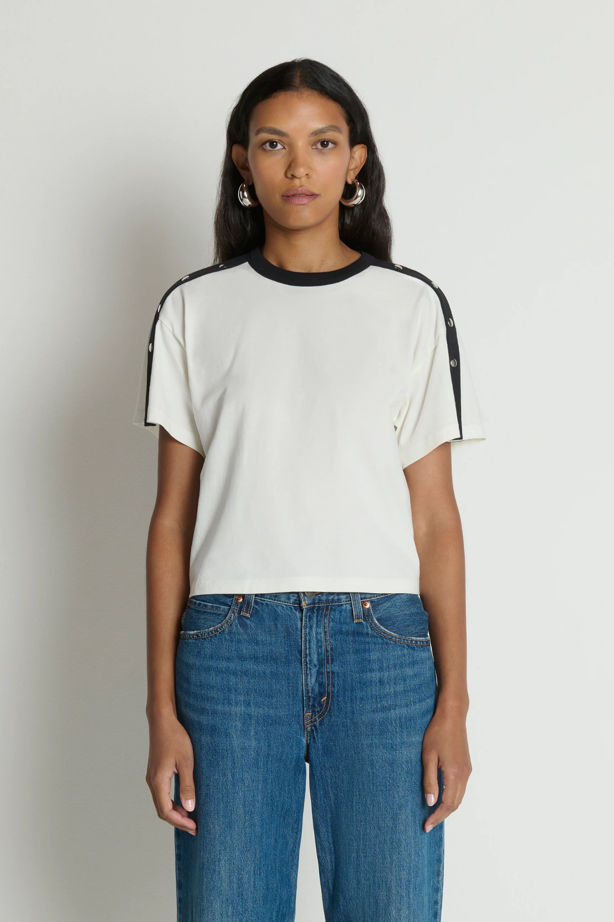 Woman wearing a white t-shirt with black accents and blue jeans on a plain background