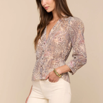 Woman wearing a patterned blouse and white pants against a beige background
