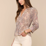 Woman wearing a patterned blouse and white pants against a beige background