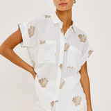 Woman wearing a white sleeveless top with shell patterns on a plain background