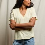 Woman wearing a light-colored top and blue jeans against a neutral background