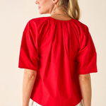 Woman wearing a red blouse and white pants against a beige background