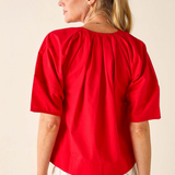 Woman wearing a red blouse and white pants against a beige background