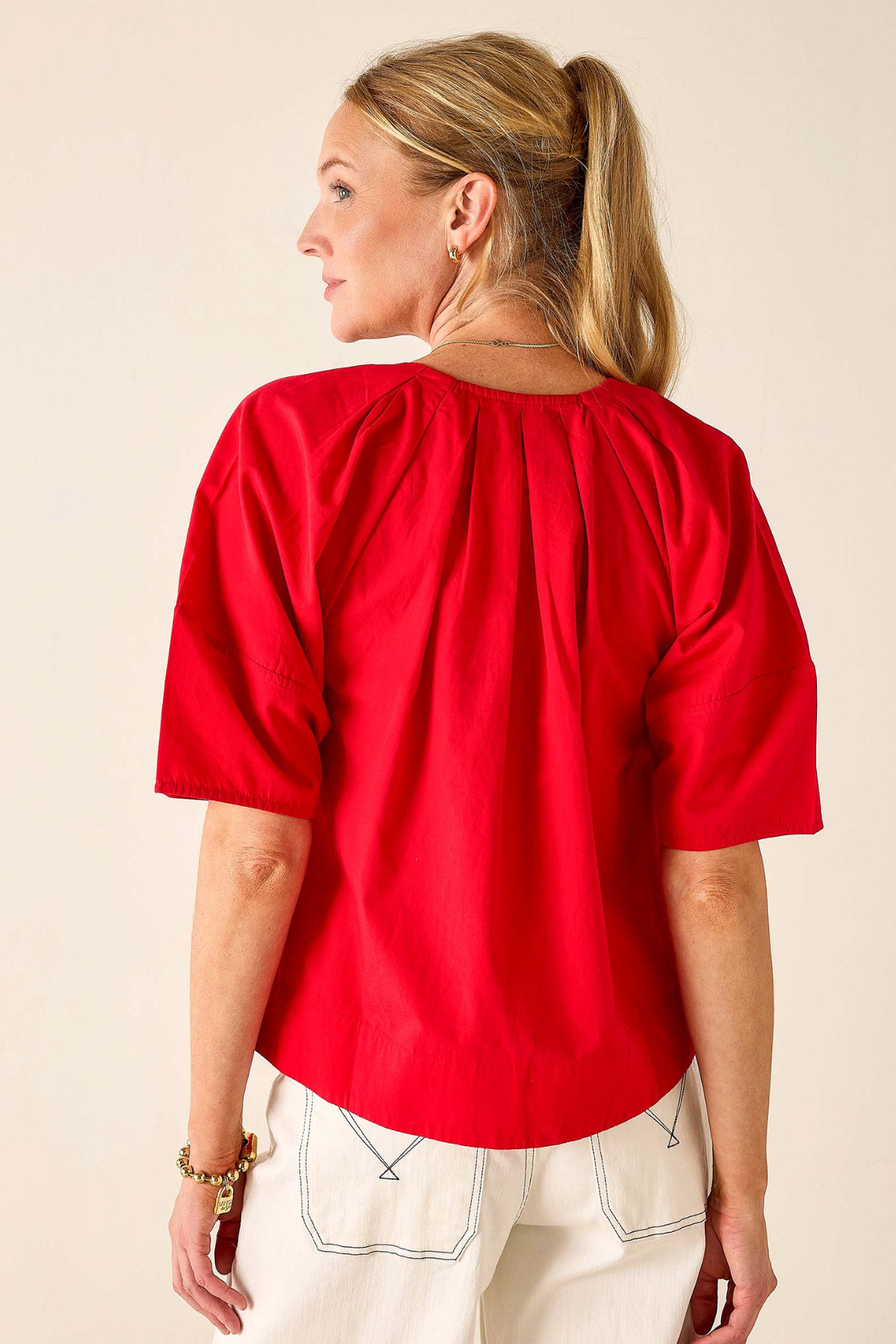 Woman wearing a red blouse and white pants against a beige background